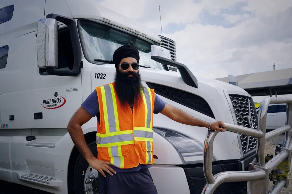 Truck driver in a high-visibility vest standing beside a white semi truck